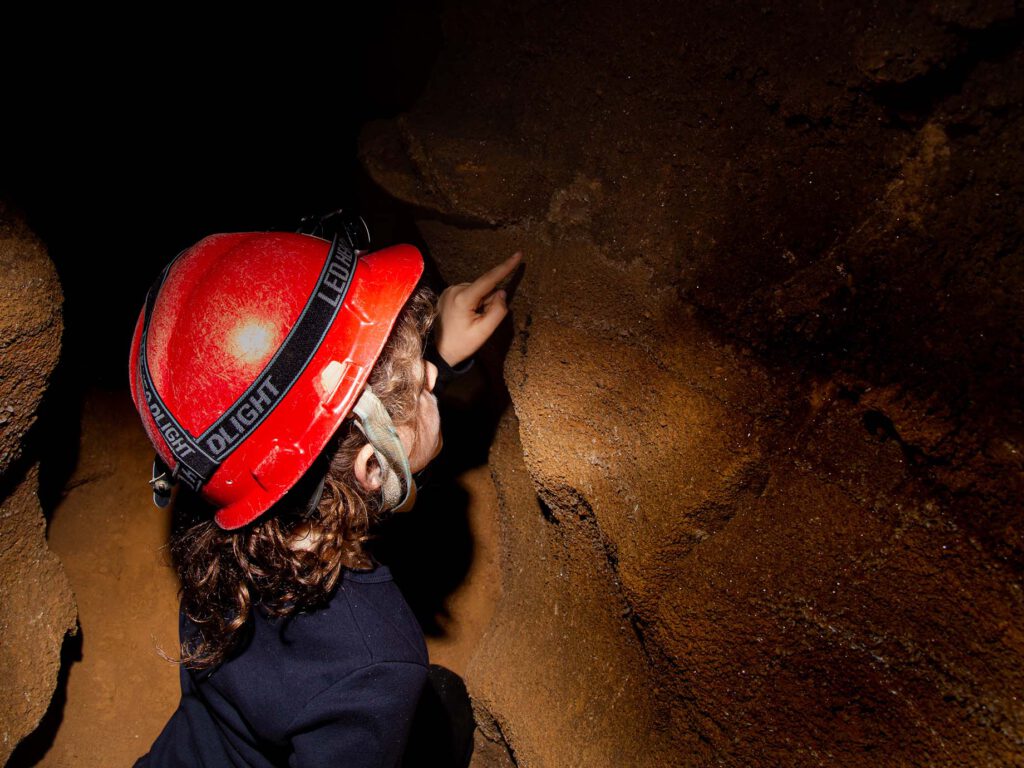 Person wearing a hat and lamp pointing at a rock in the caverns