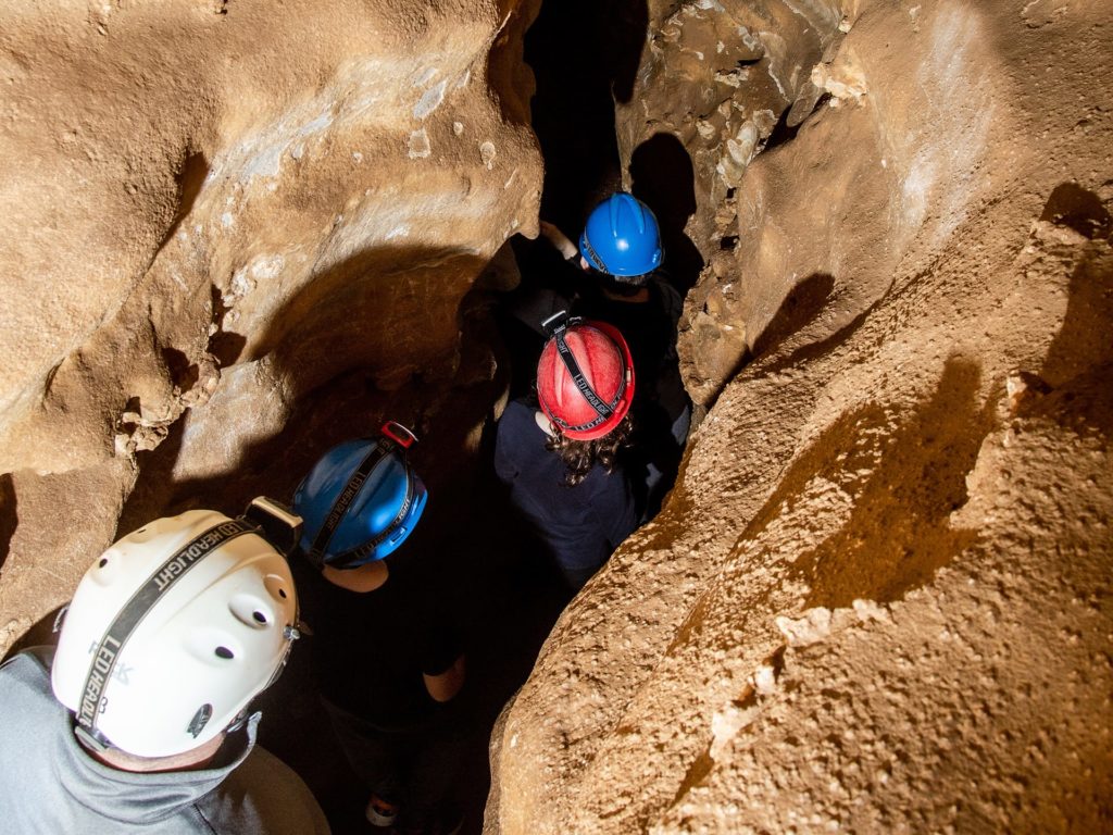 Group of kids walking through a narrow passageway on a hike through the caverns